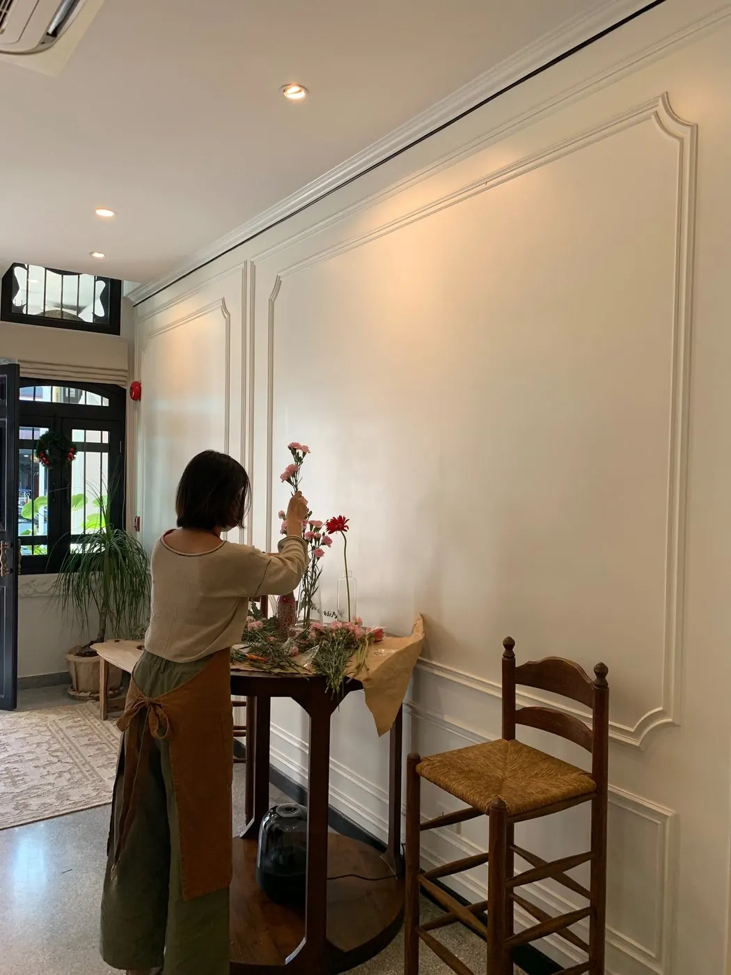 Milk from behind in an apron, arranging pink flowers in vases on a café table