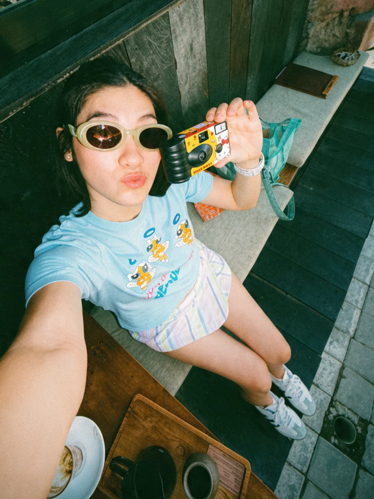 Milk holding a film camera at her café, coffee on the table beside her