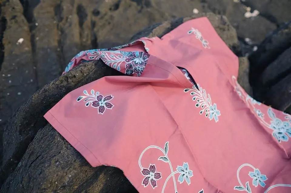 A pink Phathoongnoongdai batik piece with a floral print, laid across dark rocks