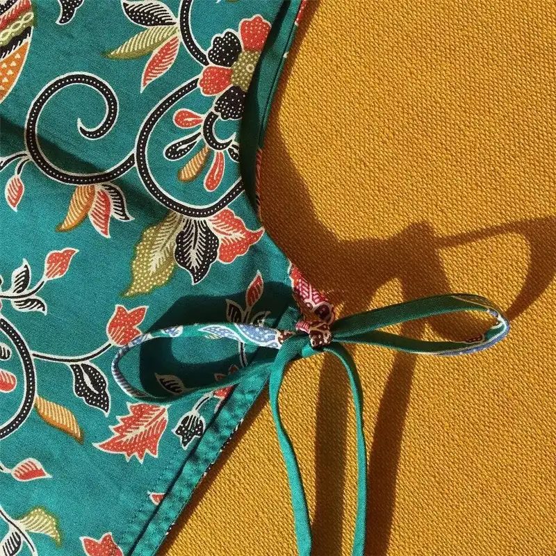 Close-up of a teal Phathoongnoongdai batik wrap with a hand-tied bow, resting on mustard linen